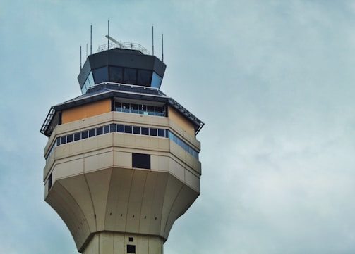 A tall, angular air traffic control tower with multiple levels and large windows, set against a cloudy sky.