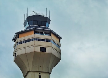 A tall, angular air traffic control tower with multiple levels and large windows, set against a cloudy sky.