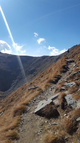 A determined hiker climbing a steep mountain path under a bright blue sky, symbolizing perseverance.