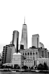 A cityscape featuring tall skyscrapers with modern architecture, including a prominent tower with an antenna spire. The image is presented in black and white, emphasizing the contrast between the architectural lines and the sky.