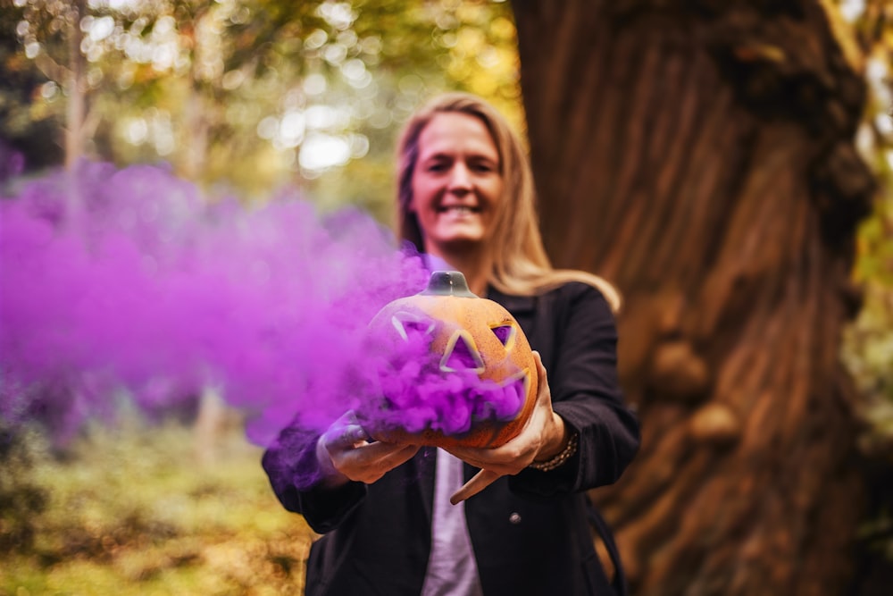 standing person holding Jack-O-Lantern emitting purple smoke