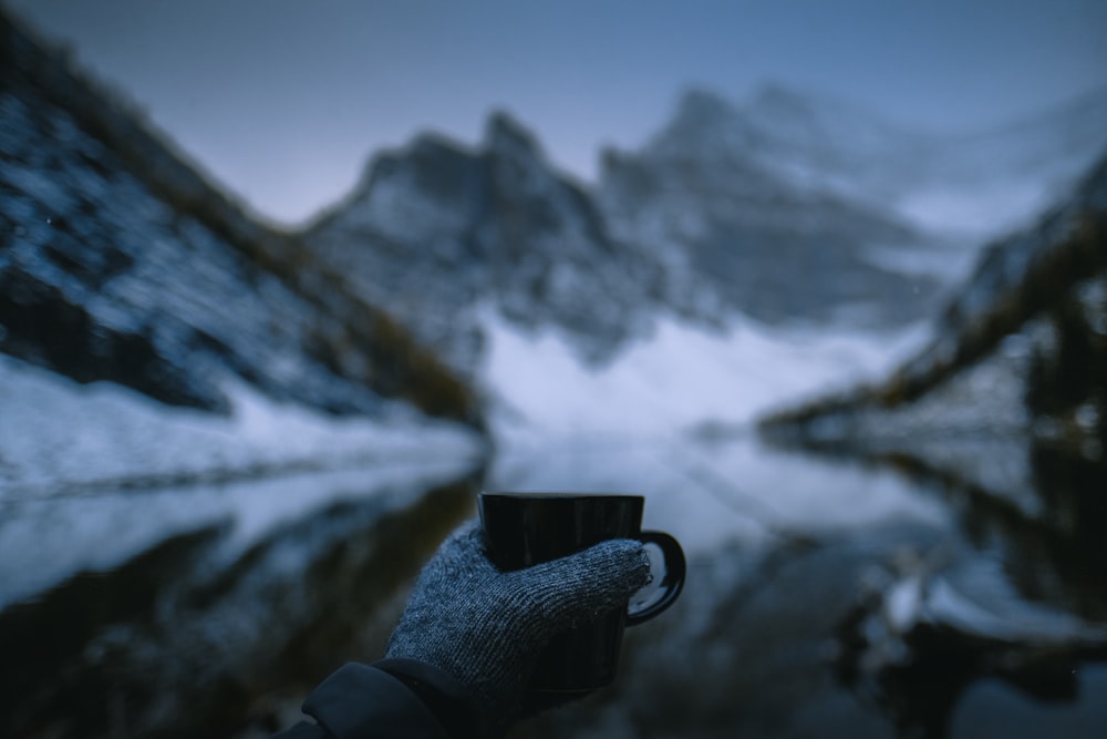 person holding mug near snow capped mountain