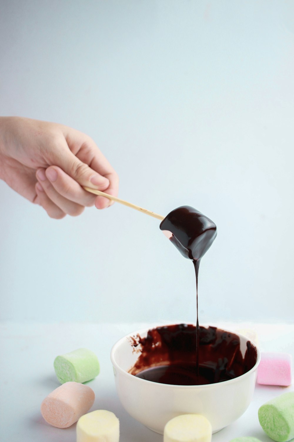 person dipping marshmallow in chocolate syrup