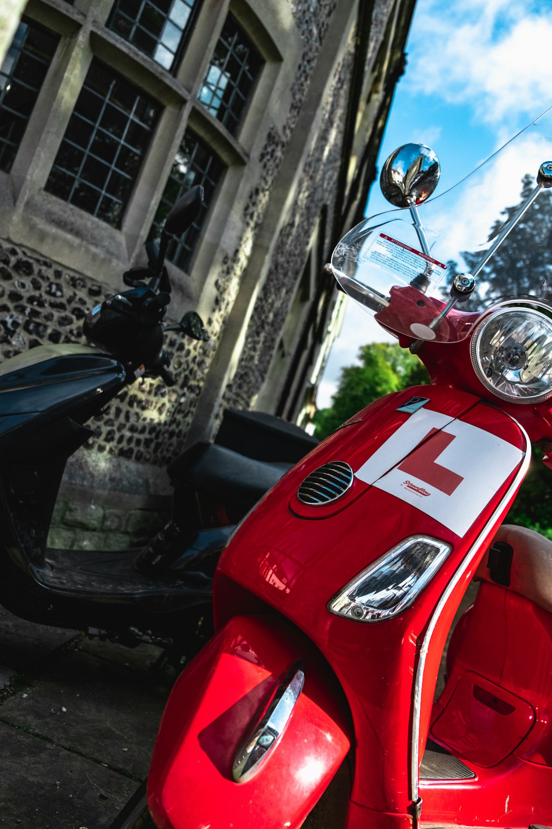 red motor scooter parked by scooter near building during daytime