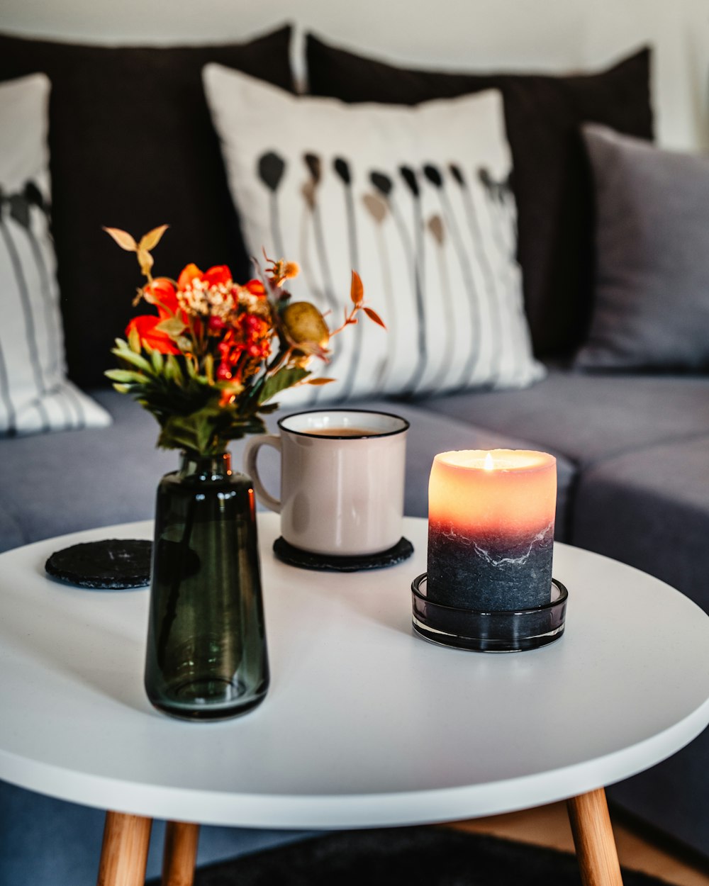 orange flower inside glass vase , lighted candle and white mug on round table