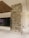 A modern interior space featuring a tall rectangular column covered in a textured tile pattern. The column is situated on a glossy white floor, and in the background, there is a large glass panel with a colorful display and overhead wooden ceiling detail.