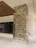 A modern interior space featuring a tall rectangular column covered in a textured tile pattern. The column is situated on a glossy white floor, and in the background, there is a large glass panel with a colorful display and overhead wooden ceiling detail.
