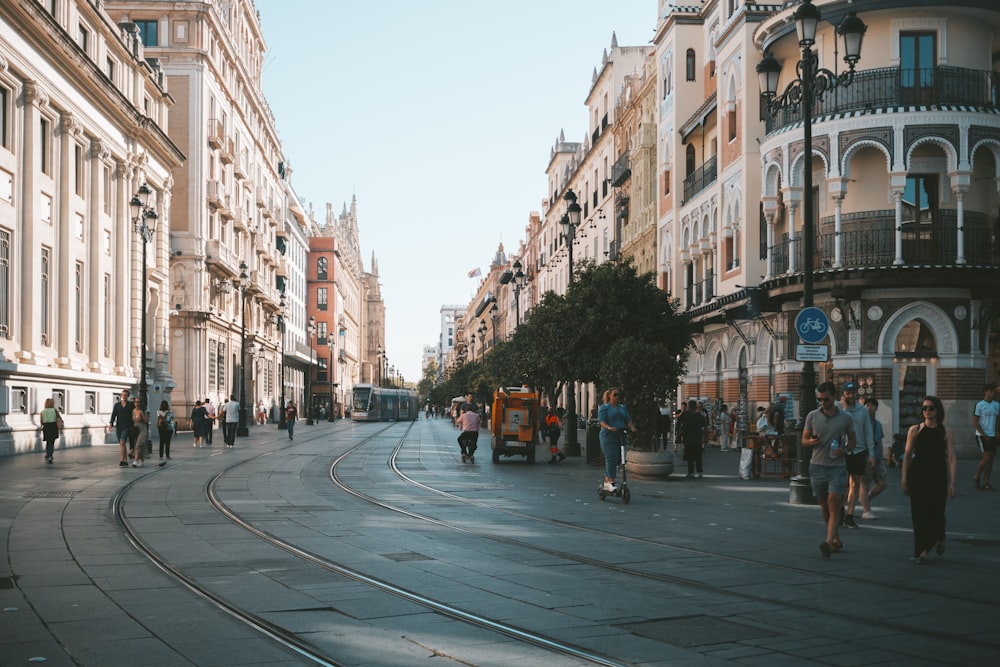 people walking on pathway near buildings and different vehicles on road during daytime