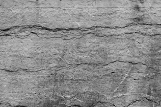 Rough textured concrete wall with visible cracks running horizontally and vertically. The surface appears weathered and aged, with various shades of gray contributing to an overall rustic and rugged look.