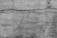 Rough textured concrete wall with visible cracks running horizontally and vertically. The surface appears weathered and aged, with various shades of gray contributing to an overall rustic and rugged look.