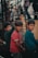 Three young boys stand together, each wearing casual clothing. The atmosphere appears earthy and muted, possibly due to the surrounding industrial or urban environment. The boys are looking towards the camera with neutral expressions.