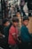 Three young boys stand together, each wearing casual clothing. The atmosphere appears earthy and muted, possibly due to the surrounding industrial or urban environment. The boys are looking towards the camera with neutral expressions.