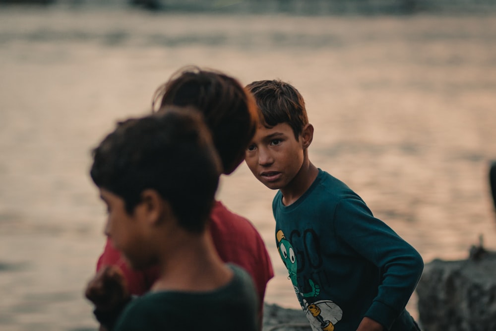 three boys standing near body of water during daytime