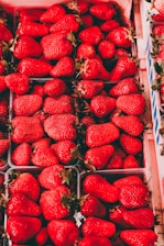A collection of vibrant red strawberries neatly arranged in cartons. The strawberries are fresh, large, and shiny with green stems. The image highlights the variety and abundance of the fruit.