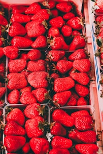 A collection of vibrant red strawberries neatly arranged in cartons. The strawberries are fresh, large, and shiny with green stems. The image highlights the variety and abundance of the fruit.