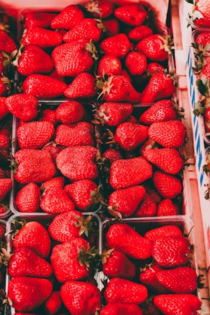 A collection of vibrant red strawberries neatly arranged in cartons. The strawberries are fresh, large, and shiny with green stems. The image highlights the variety and abundance of the fruit.