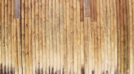 Vertical wooden planks aligned closely together create a textured pattern with varying shades of natural wood grain. The surface appears weathered, with some planks showing darker areas due to age or exposure.