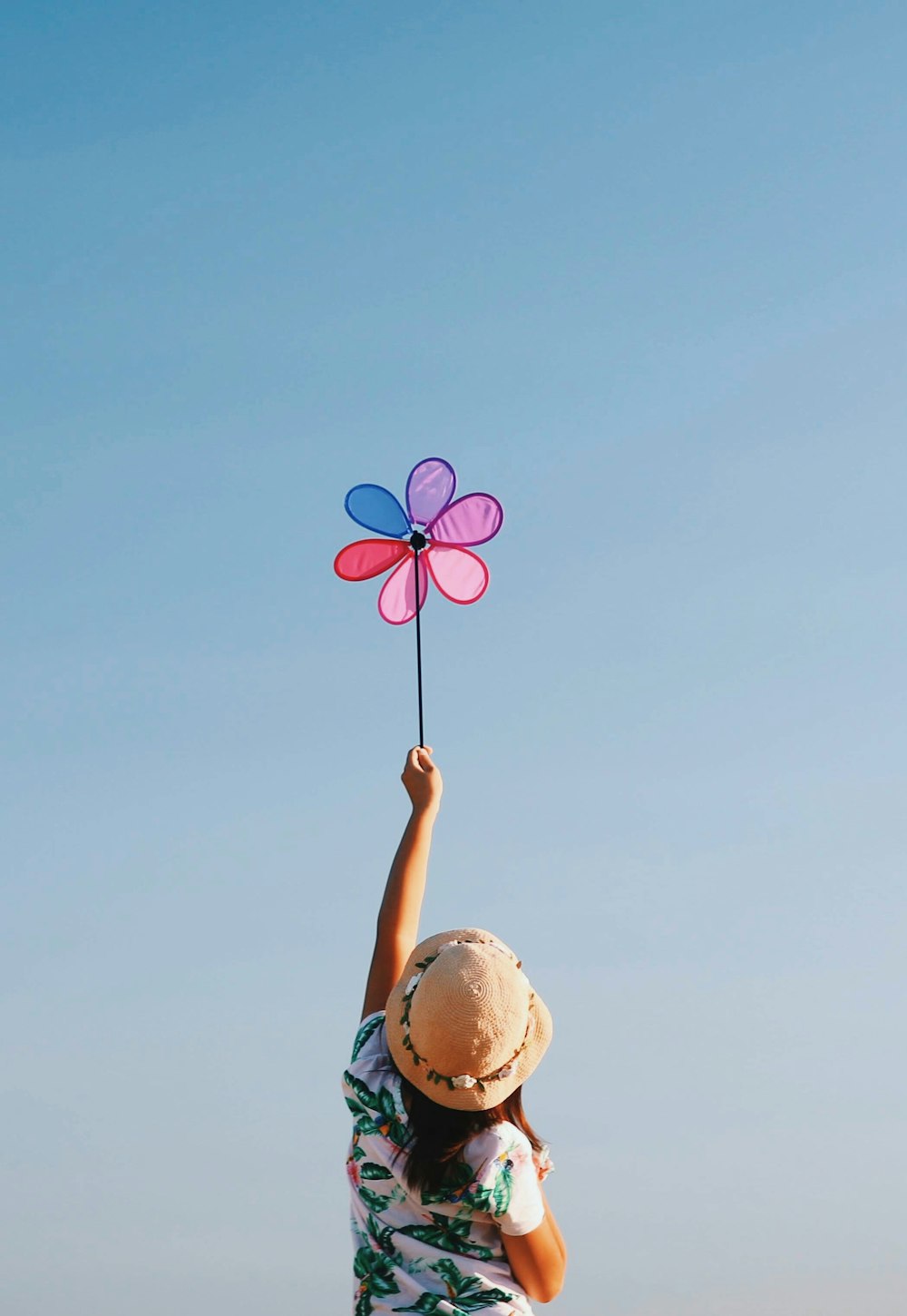 woman in floral shirt and brown sun hat holding multicolored flower