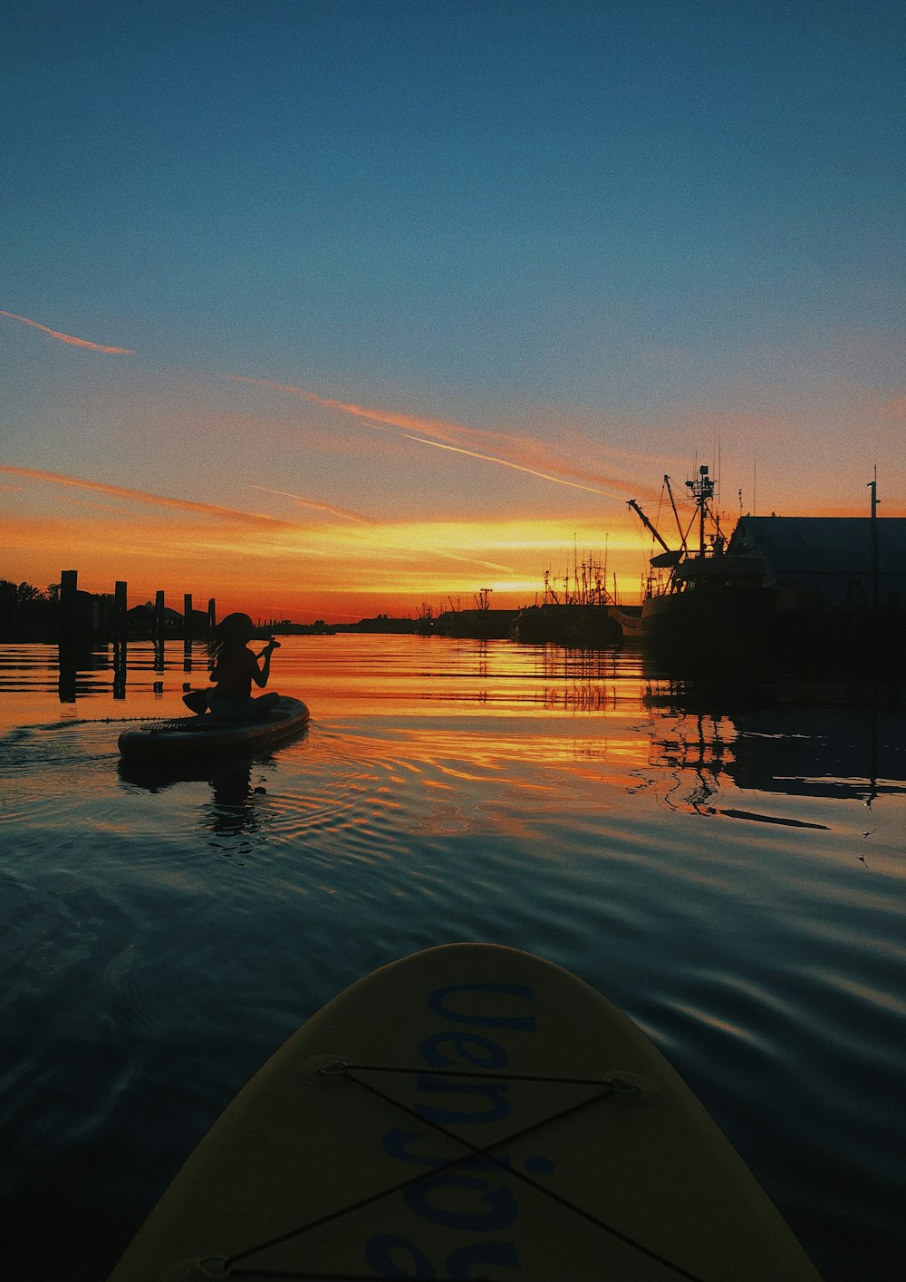 woman sits on paddleboard during sunset