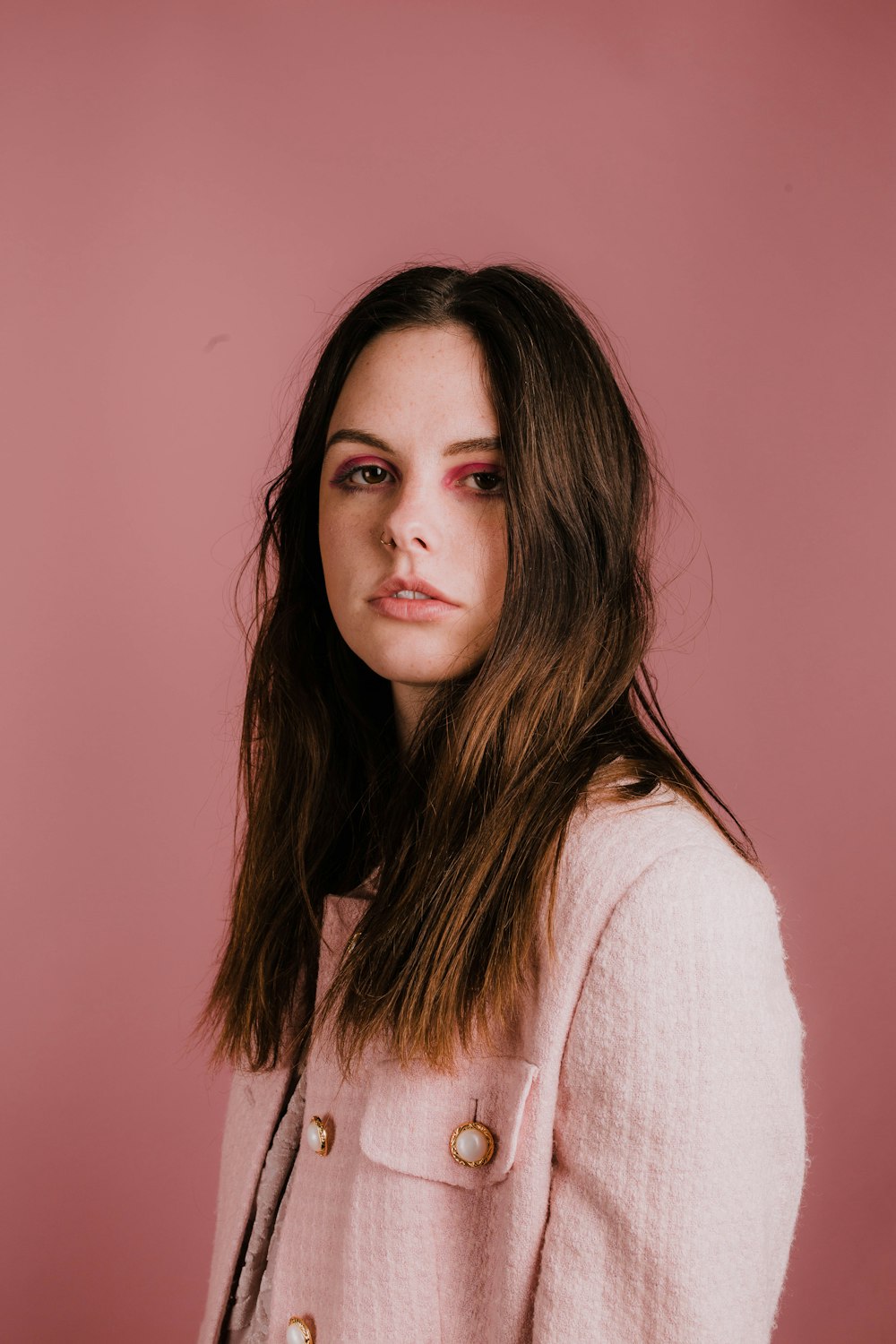 woman wears white coat on pink background