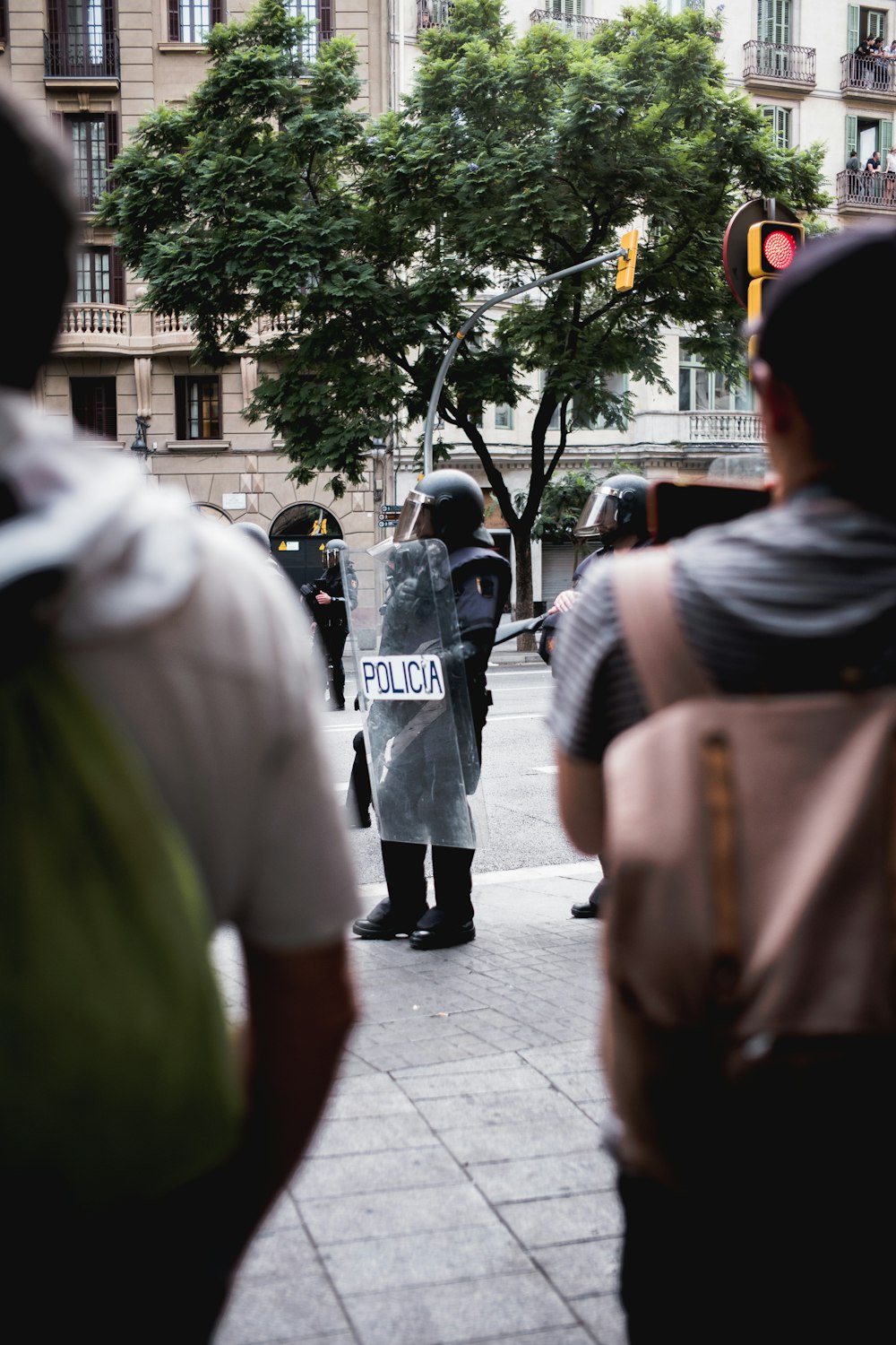 people carrying backpack standing near police with shield