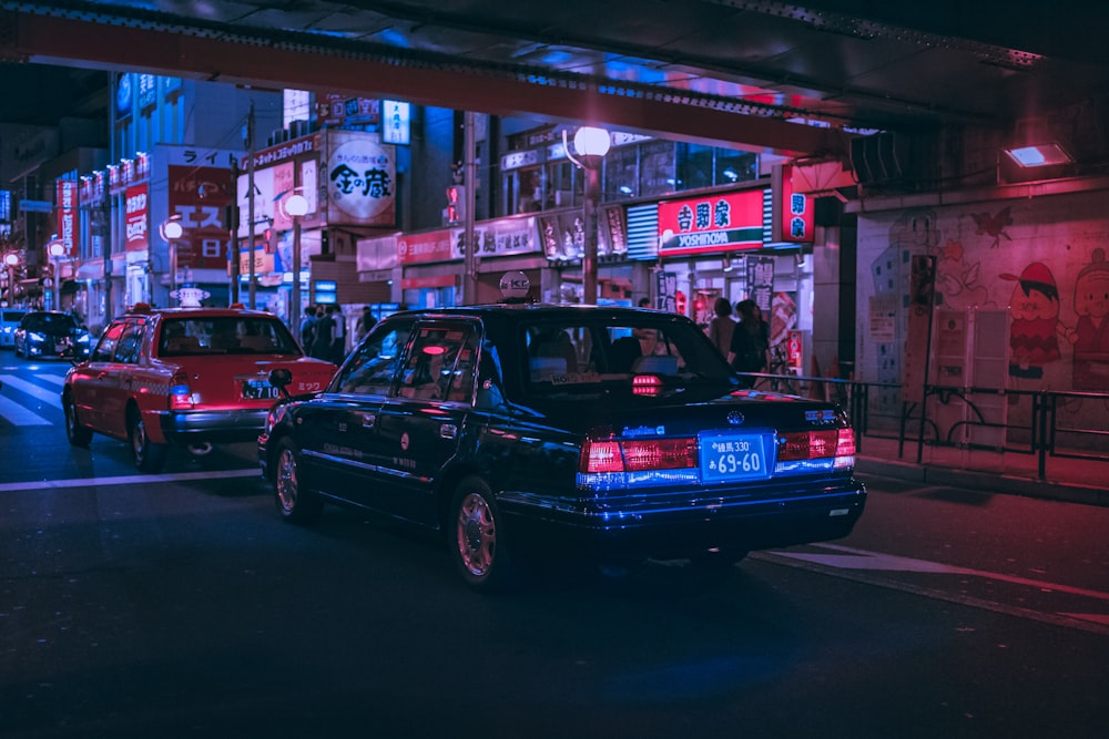 people walking on pathway near buildings and different vehicles on road during night time