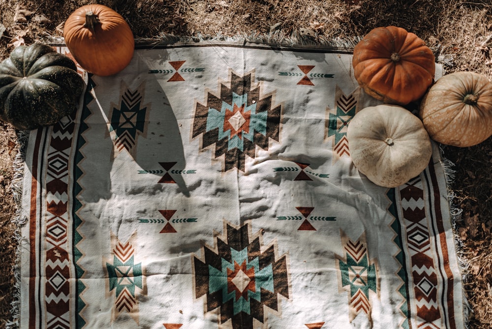 five white and orange pumpkins on white and multicolored tribal mat
