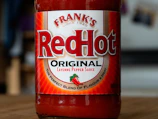 Bright red hot sauce bottles with fresh chili peppers around them.