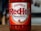 A bottle of Frank's RedHot Original Cayenne Pepper Sauce, featuring a bold red label with white and red lettering. The label also includes a graphic of chili peppers and text stating 'The Perfect Blend of Flavour & Heat'. The bottle sits on a wooden surface with a blurred background.