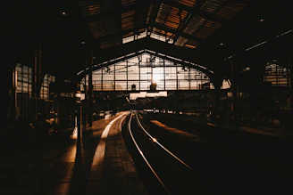 A rain-speckled window overlooking a dimly lit train station at twilight