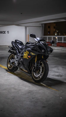 A sleek black motorcycle with gold accents parked beside a luxury airport terminal at sunset.