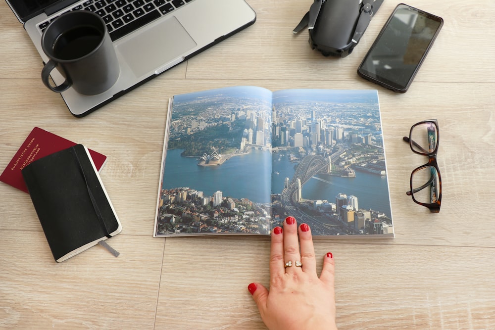 city and sea graphic opened book beside eyeglasses and laptop