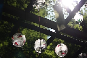A delicate garden wind chime swaying gently in the breeze with sunlight filtering through leaves.