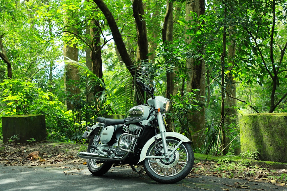 black and gray motorcycle on road surrounded with tall and green trees during daytime