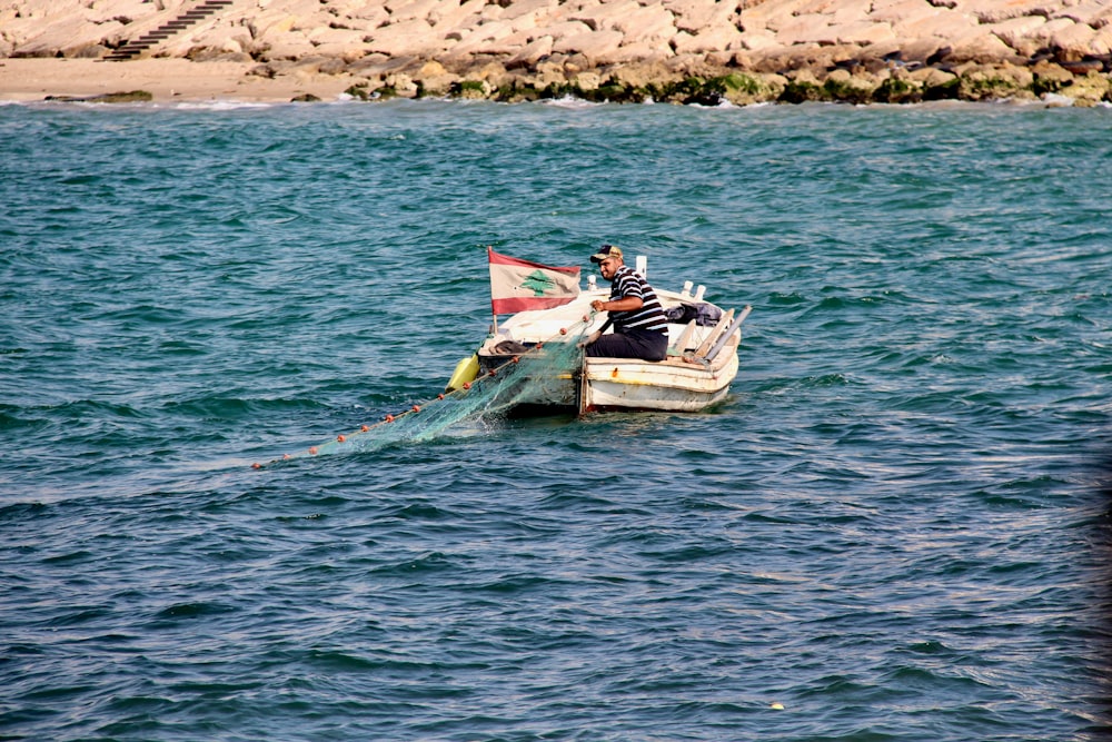 man wearing black and gray striped shirt sitting on white boat on blue body of water during daytime