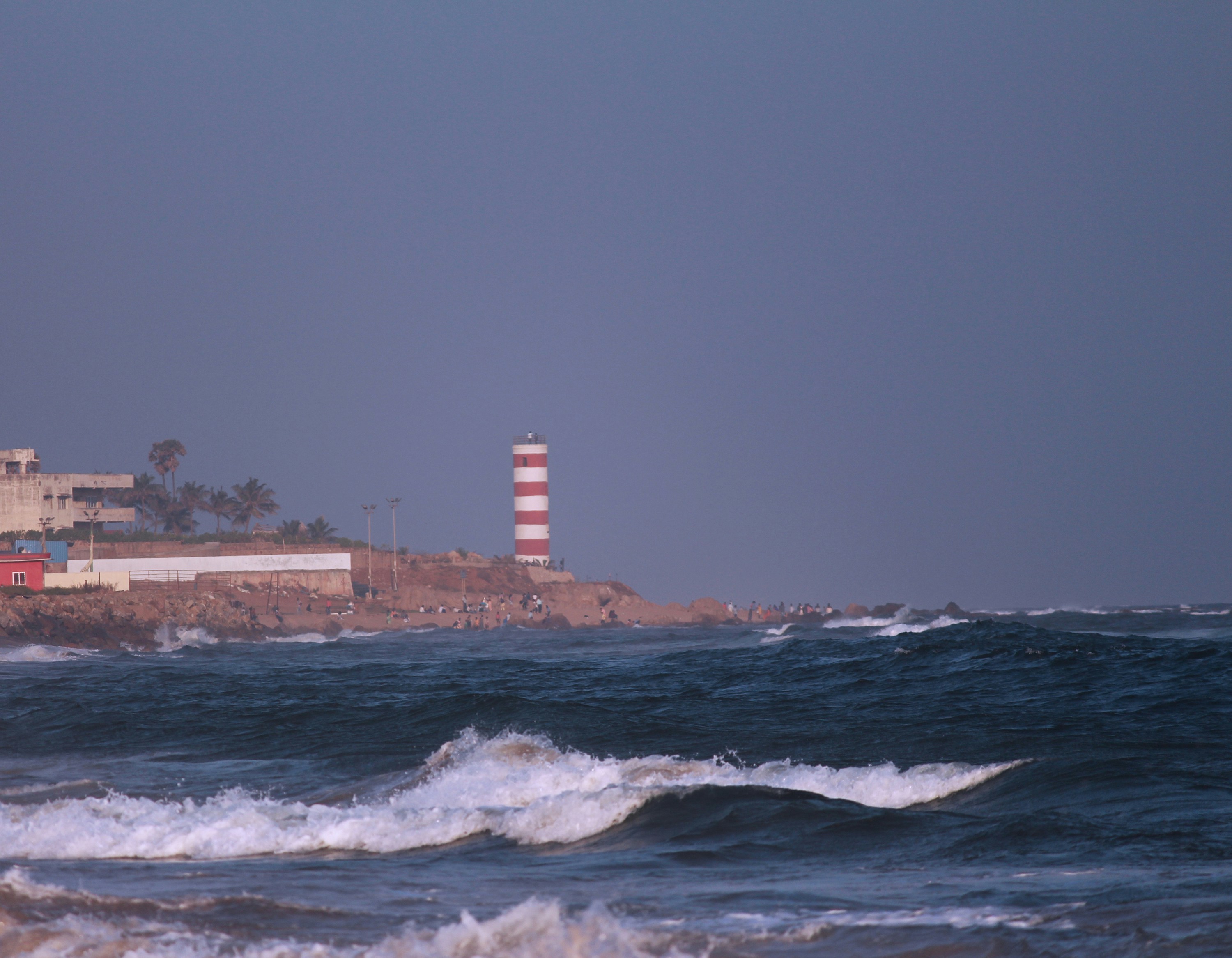 Isang parola na nagniningning sa sinag nito sa isang mabagyong gabi, na may malalaking alon na humahampas sa mga bato.