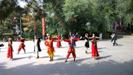 Performers in colorful costumes performing a dynamic group choreography outdoors.