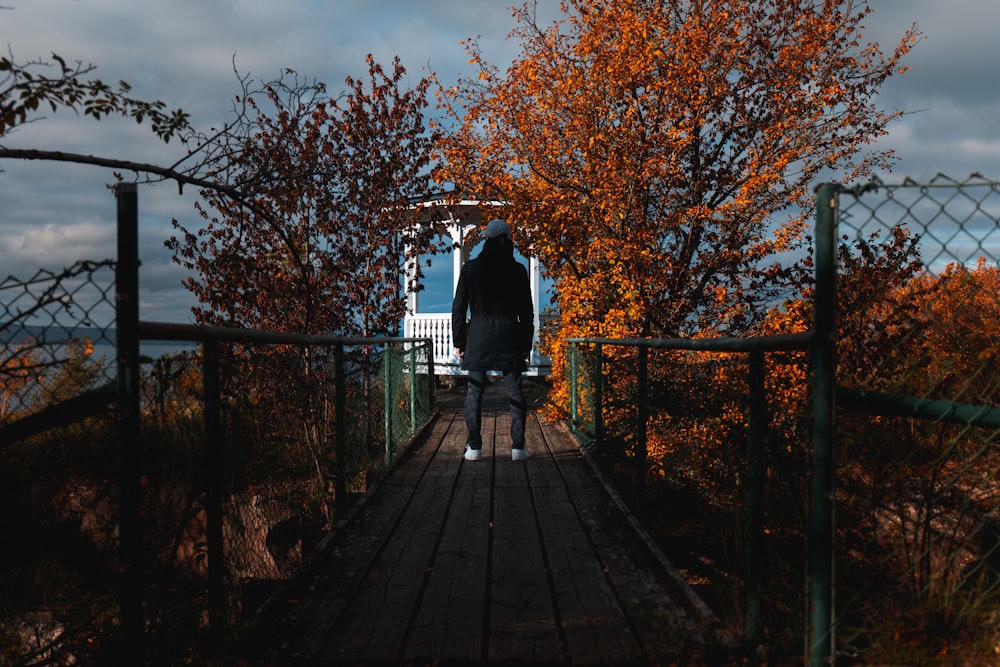 person standing on wooden footbridge near white gazebo under blue and white sky during daytime