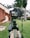 A camera mounted on a tripod is positioned on a grassy area. The camera's screen is visible, capturing a building with red and beige walls and surrounded by tall palm trees. The angle suggests a focus on outdoor photography.