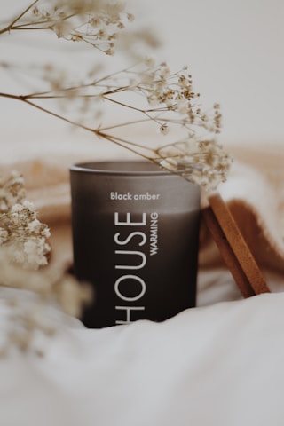 A sophisticated black and gold candle glowing softly on a white marble surface with subtle hints of aromatic mist.