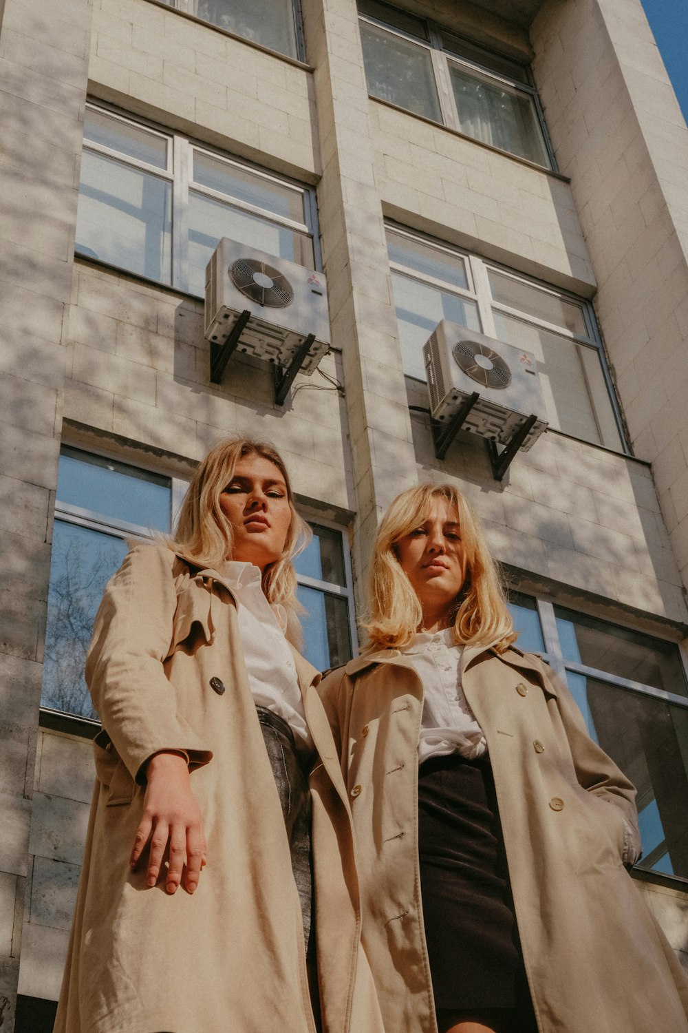 two women wear overcoats outside the building