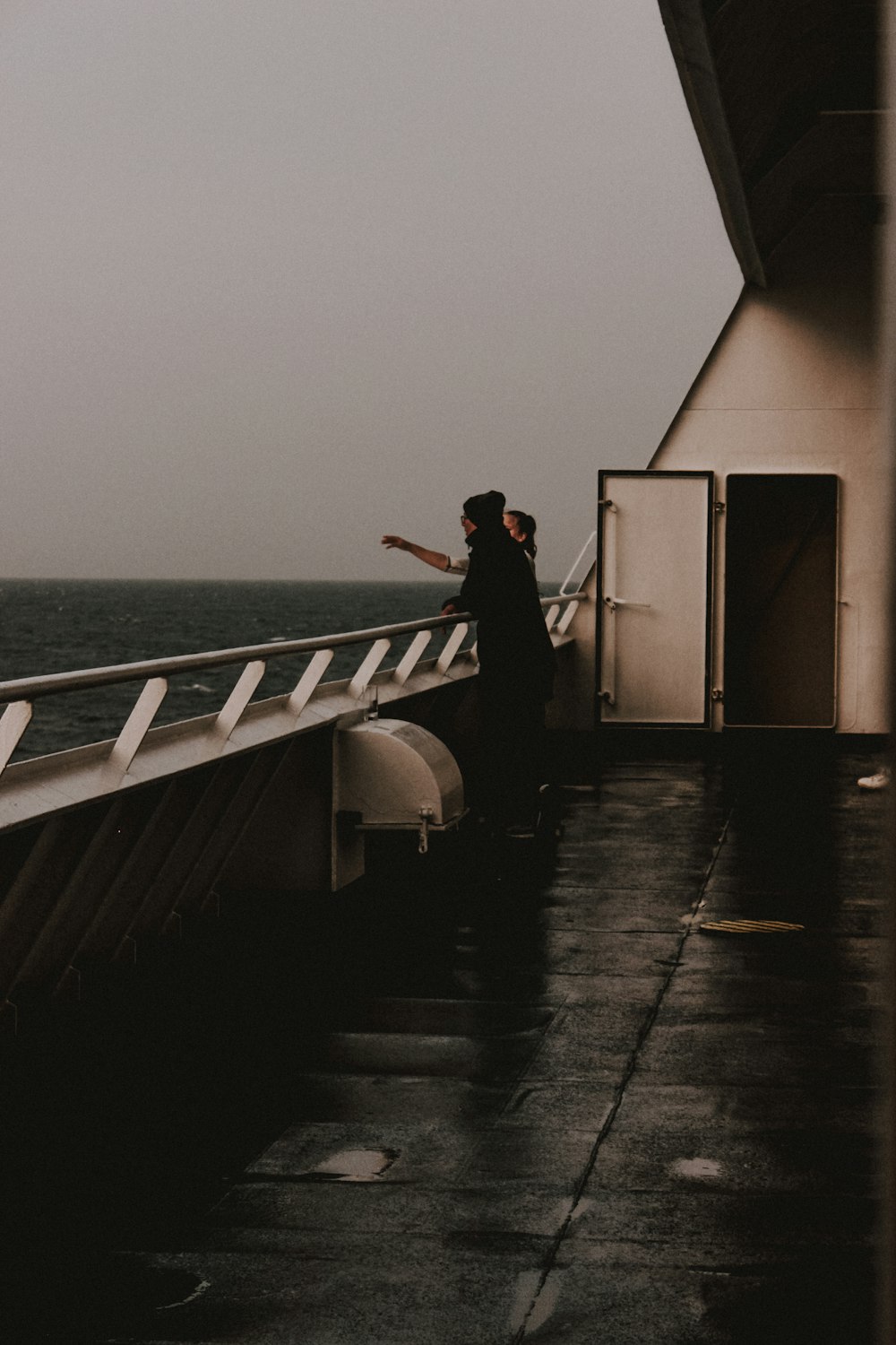 two persons standing on railing of a ship during day