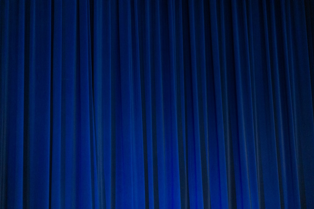 Un homme en costume et cravate debout devant un rideau bleu