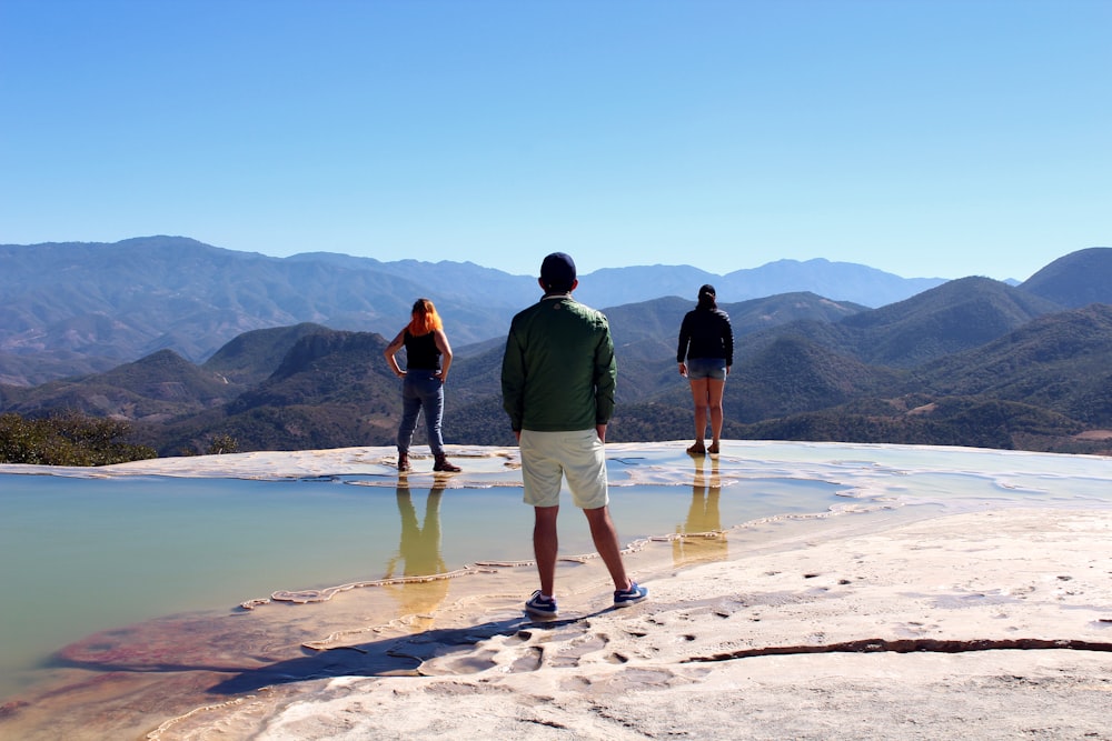 three person standing on seashore