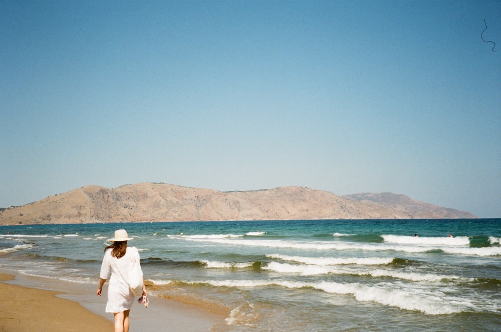 흰 드레스와 모자를 쓰고 해변을 걷는 여자