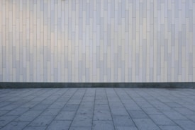 A geometric pattern consisting of vertical rectangular tiles arranged in an offset layout covers the wall, creating a minimalist and modern appearance. The floor features large, square gray tiles laid out in a grid pattern, complementing the wall's design.