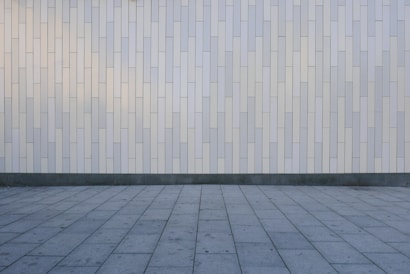 A geometric pattern consisting of vertical rectangular tiles arranged in an offset layout covers the wall, creating a minimalist and modern appearance. The floor features large, square gray tiles laid out in a grid pattern, complementing the wall's design.