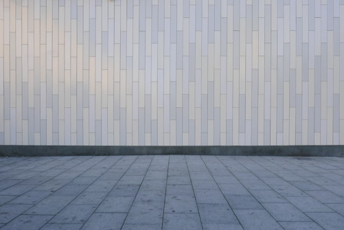 A geometric pattern consisting of vertical rectangular tiles arranged in an offset layout covers the wall, creating a minimalist and modern appearance. The floor features large, square gray tiles laid out in a grid pattern, complementing the wall's design.