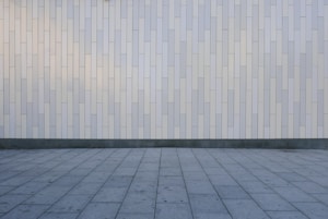 A geometric pattern consisting of vertical rectangular tiles arranged in an offset layout covers the wall, creating a minimalist and modern appearance. The floor features large, square gray tiles laid out in a grid pattern, complementing the wall's design.