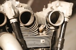 An intricate view of a mechanical engine, showcasing cylinder heads and cooling fins in close detail. The image highlights the metallic textures and complex shapes, with prominent pipes and bolt details.